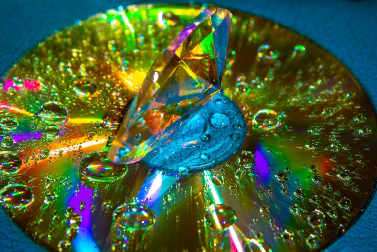 A prism diamond on a CD reflects rainbow colors, with water droplets enhancing the light display.